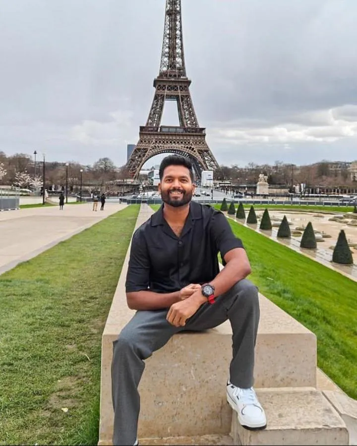 A man sits on a bench, gazing at the Eiffel Tower, surrounded by the beauty of Paris on a sunny day.