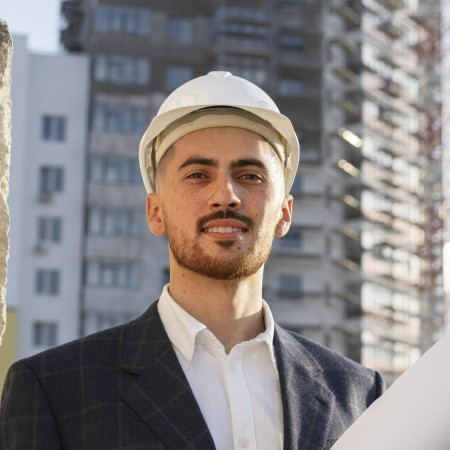 An engineer with white hat and carrying blueprint.